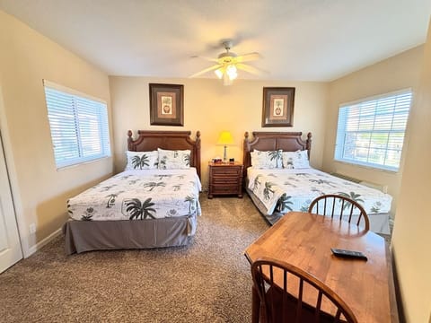Spacious bedroom featuring two comfortable beds, ceiling fan, small dining/work table, and plenty of natural light.