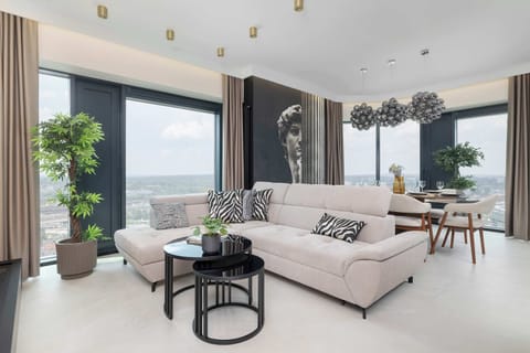 Bright and spacious modern living room with floor-to-ceiling windows, a comfortable sectional sofa, and stunning city views. Perfect for relaxing after a day of exploring.