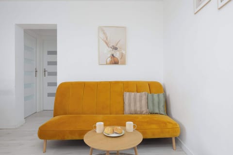 A cozy living room with a mustard-yellow sofa and a small coffee table. The bright interior has a modern and welcoming feel.