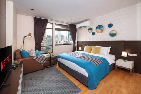 Thai-inspired design from local makers. The bedroom features a TV, curtain to block out light, a sofa with a standing lamp, and an oversized wardrobe. The power outlets on both sides of the bed, you can charge your phone without unplugging the lamp.