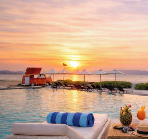 Sunset infinity pool with beach loungers, bar van & ocean views