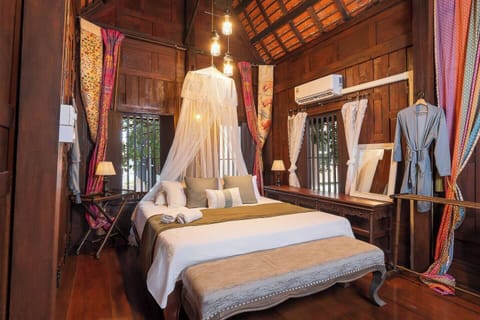 【Bed 1】Blending Thai tradition with comfort, featuring a ceiling fan, AC, a mosquito net, and a cozy bathrobe for lounging. You can choose to open the anti-insect covered windows during the night to experience the full Thai living. 