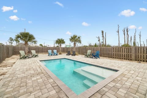 A private pool surrounded by paver stones and colorful Adirondack chairs awaits beneath clear blue skies, framed by palm trees and a secure privacy fence.