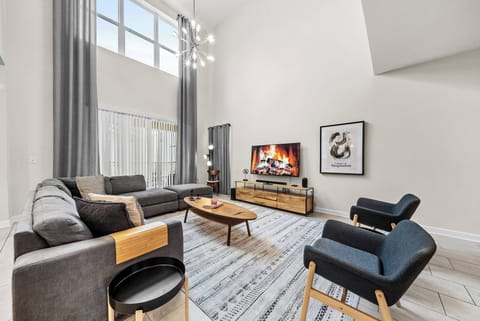 The inviting living room boasts a plush gray sectional and chic black armchairs for your comfort. High ceilings and large windows fill the space with natural light, while the modern decor enhances the sophisticated ambiance.