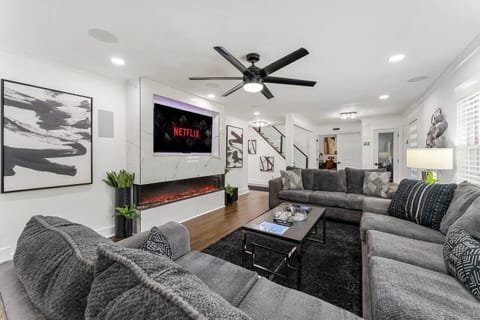 Stylish living room, complete with a large sectional, a sleek wall-mounted TV, and a modern electric fireplace. Perfect for unwinding after a day of work or exploring the city. Business travelers and leisure guests alike will love the ambiance.