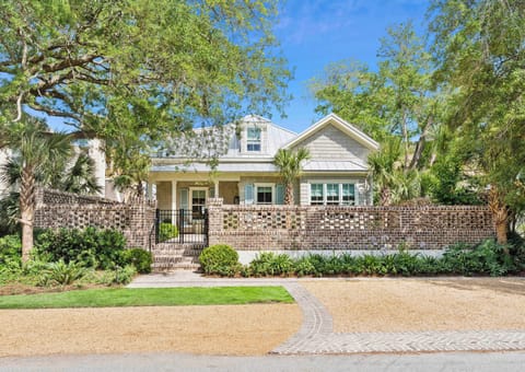 Charming coastal cottage featuring classic brick detailing, inviting front porch, and lush tropical landscaping with mature palms and oak trees in a peaceful neighborhood setting.