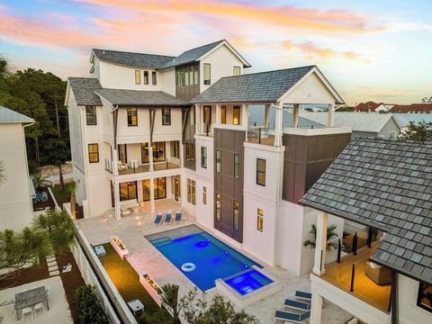 A stunning multi-level vacation home showcasing modern coastal architecture with an inviting pool and spacious outdoor areas, set against a beautiful sunset backdrop in a peaceful residential neighborhood.