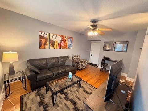 Cozy living room w/ leather sofa, smart TV, ceiling fan, and dining nook.