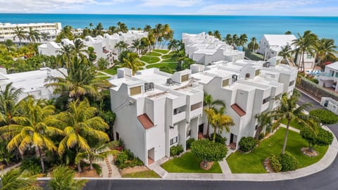 Aerial Property View: The complex sits steps from the open Atlantic, with white-roofed buildings clustered around green lawns and turquoise water stretching to the horizon.