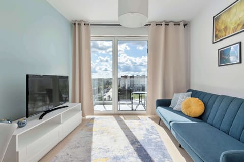 Bright and welcoming living room with a comfortable sofa, flat-screen TV, and large windows providing plenty of natural light.