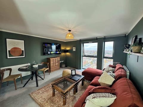 Sink into the plush rust-red sectional sofa in this stylishly decorated living space. An ornate carved wooden coffee table, vintage patterned rug, and dark-green accent walls blend character with comfort — perfect for relaxing evenings in.