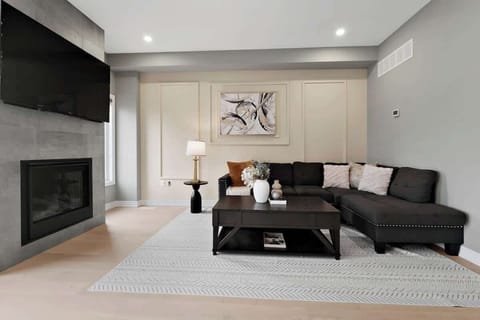 Stylish living space with a cozy sectional sofa, chic throw pillows, sleek fireplace, large smart TV, elegant coffee table, modern lamp, and wall art.
