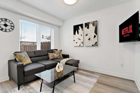 Chic living area with plush sectional sofa, stylish throw pillows, elegant glass coffee table, modern wall art, large window, and wall-mounted TV.