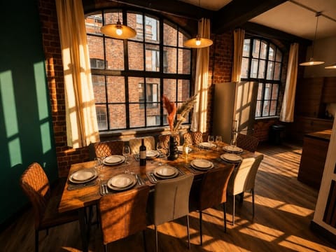 Spacious dining area with a large table ideal for group meals, framed by exposed brickwork and impressive industrial-style windows bringing in plenty of natural light.