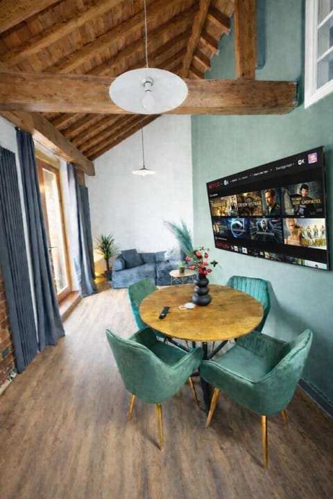 Stylish open-plan living and dining area with Smart TV and Netflix, dining table for 4, and comfortable seating. High ceilings with exposed wooden beams and access to a private balcony make the space bright and relaxing.