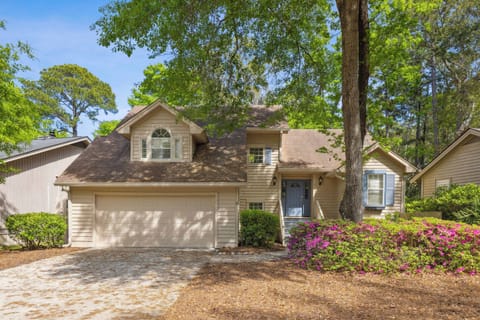 Vibrant azaleas frame the entryway to this peaceful home, where dappled afternoon glow filters through the towering oak trees. Soft taupe siding and slate blue shutters create a charming facade that promises a quiet, airy stay.