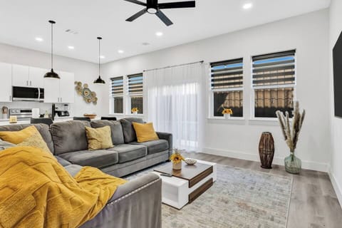 Bright and stylish living room with a cozy sectional sofa, smart TV, and open layout leading to the kitchen. Perfect for relaxing, watching movies, or enjoying time together.
