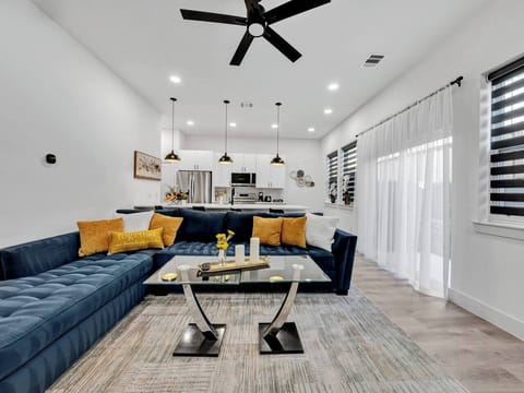 Bright and stylish living room with a cozy sectional sofa, smart TV, and open layout leading to the kitchen. Perfect for relaxing, watching movies, or enjoying time together.