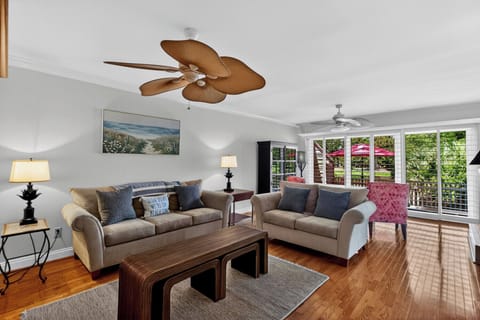 Unwind in your bright, airy living room with inviting sofas and tropical ceiling fans. Sliding doors open to a private balcony where lush greenery and natural light create a peaceful retreat.