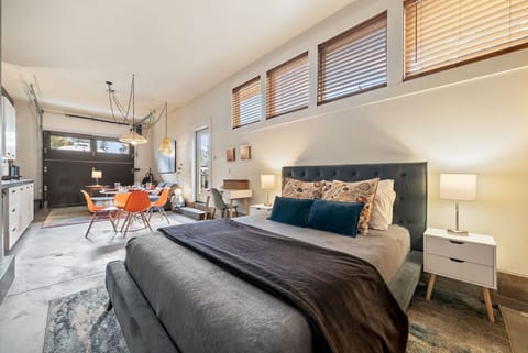 Your open-concept retreat blends bedroom comfort with living space convenience. Natural light pours through high windows, illuminating stylish furnishings, a plush bed, and a cozy dining nook—everything you need to unwind and feel at home.