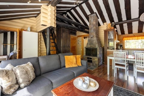 Sink into the plush grey corner sofa beside the wood-burning fireplace, framed by exposed timber beams for an authentic Lapland cabin feel.