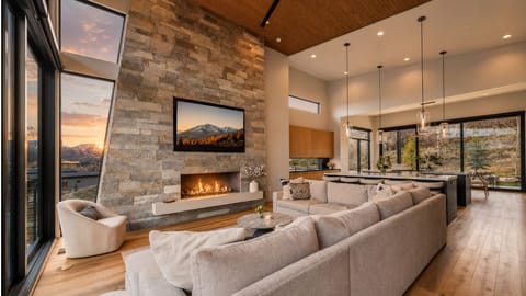Gather around the dramatic stone fireplace in the open-concept great room, featuring soaring ceilings, plush seating, and panoramic mountain views.