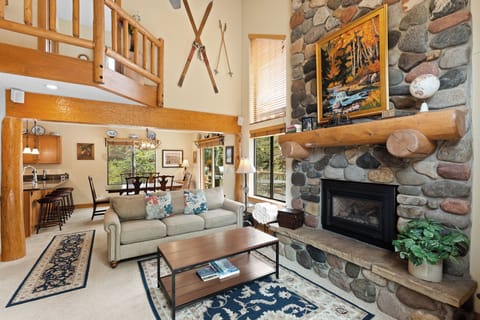 Unwind in this soaring living room where rustic log beams meet a stunning stone fireplace. Your cozy retreat opens to the kitchen and deck, blending mountain charm with modern comfort.