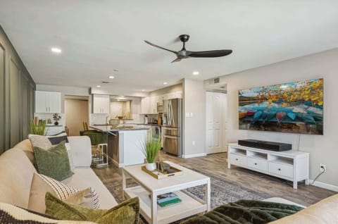 The living room flows seamlessly from the kitchen, anchored by a bold sage green accent wall, plush sectional, large Smart TV, and sliding glass doors opening to the private patio.