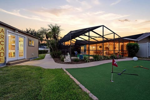 The lit-up ARCADE sign, the putting green in front, and the screened pool glowing behind it — the full picture of what's in the backyard at night.