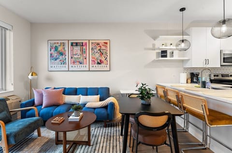 Bright and stylish living space with colorful wall art, cozy seating, and an open layout connected to the kitchen.