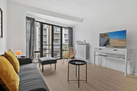 Comfortable living room with a cosy sofa, bright accent cushions, smart TV and large windows — relax and unwind in this Knokke apartment near the beach.