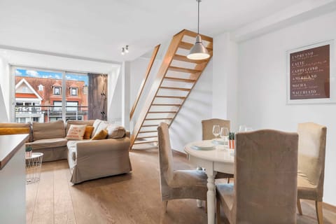 Open-plan living and diningFully equipped modern kitchen with white cabinetry, wood worktop, oven and microwave. Knokke vacation duplex. area with comfy sofa and the duplex staircase – light-filled lounge in Knokke.