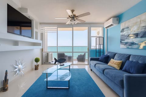 Bright and modern oceanfront living room featuring a comfy sofa, glass coffee table, and breathtaking sea views from the balcony—perfect for relaxing after a day in the sun.