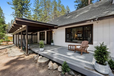 Front porch with a wooden Adirondack chair on a gray deck, shaded by a dark brown pergola roof.