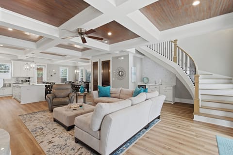 Soaring coffered ceilings crown your open-concept living space, where elegant furnishings invite you to unwind. Natural light floods the home, highlighting warm wood floors and the graceful staircase.