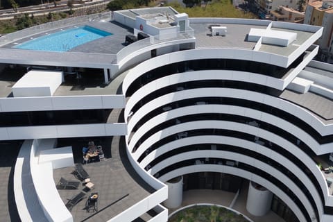 Black lounge chairs circle the rooftop pool, set within the building's signature curved architecture.