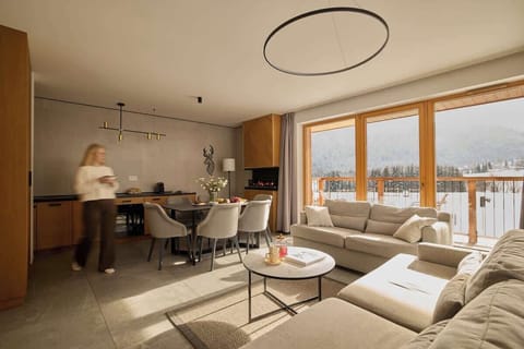 Salon urządzony jest w nowoczesnym, przytulnym stylu i pełni funkcję centralnej części apartamentu. Dwie rozkładane sofy z funkcją spania zapewniają komfortowe miejsca noclegowe, a kominek podkreśla górski charakter wnętrza.