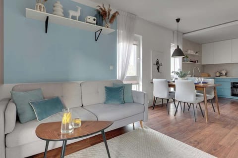 W salonie znajduje się rozkładana sofa pełniąca funkcję dodatkowego miejsca do spania, projektor z kanałami kablowymi i Smart TV oraz stół jadalniany z krzesłami.