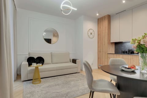 Elegancki salon z aneksem kuchennym zachwyca jasnym, nowoczesnym wystrojem i przytulną atmosferą. Stylowe detale, wygodna sofa oraz funkcjonalna przestrzeń tworzą idealne miejsce do relaksu i wspólnych posiłków.