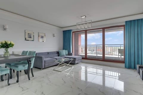 Przestronny i jasny salon zachwyca eleganckim wystrojem w odcieniach bieli i granatu. Znajduje się tu wygodna, rozkładana sofa, stolik kawowy oraz telewizor z dostępem do kanałów i funkcją Smart TV.