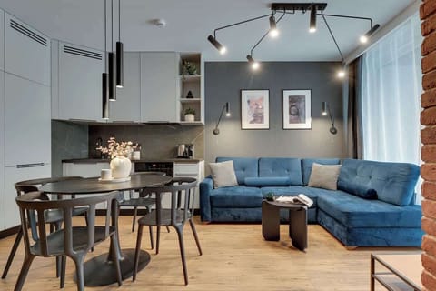Nowoczesny salon z aneksem kuchennym, elegancką strefą jadalnianą oraz komfortową, rozkładaną sofą. Stylowe oświetlenie, designerskie detale i przestronny układ tworzą idealne miejsce do relaksu i wspólnego spędzania czasu.
