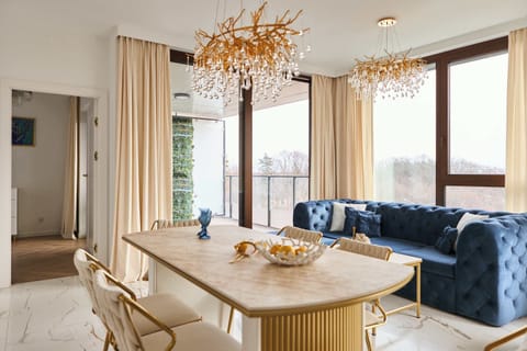 Przestronny salon utrzymany jest w eleganckim, jasnym stylu glamour. Centralnym punktem pomieszczenia jest duża, granatowa sofa z możliwością rozłożenia, idealna do wypoczynku lub jako dodatkowe miejsce do spania.