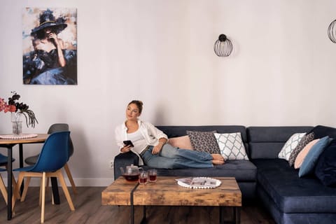 Stylowy salon z granatową sofą i designerskimi dodatkami tworzy przytulną przestrzeń do relaksu. Jasne wnętrze z drewnianymi akcentami oraz częścią jadalnianą zapewnia komfortowy pobyt w nowoczesnym apartamencie.