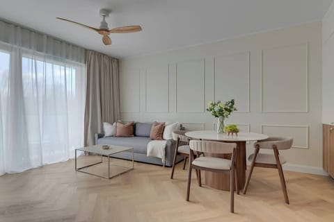 Stylowy salon w jasnych barwach oferuje komfortowy wypoczynek dzięki rozkładanej sofie oraz dużemu telewizorowi z funkcją Smart TV.
