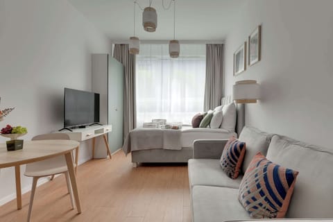 Przytulne studio urządzone w jasnych, naturalnych barwach, łączące komfortową strefę wypoczynkową z funkcjonalnym aneksem jadalnianym. Duże okna zapewniają dużo światła, tworząc idealne miejsce na relaks i pobyt w mieście.
