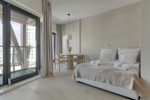 Elegancka strefa wypoczynkowa z dużym łóżkiem i miejscem do wspólnego relaksu tworzy jasną, harmonijną przestrzeń. Naturalne materiały, subtelne kolory i balkon nadają wnętrzu wyjątkowo przytulny klimat.