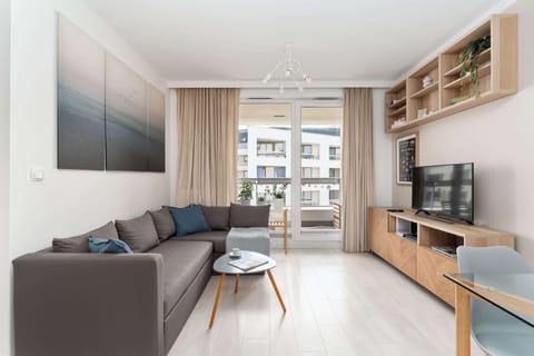Centralną częścią apartamentu jest salon z rozkładaną sofą, telewizorem z kanałami kablowymi i funkcją Smart TV oraz wyjściem na balkon. Duże przeszklenia zapewniają wnętrzu dużo naturalnego światła.
