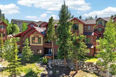 Mountain-style architecture surrounded by tall pines and natural rock gardens creates a serene alpine village setting.