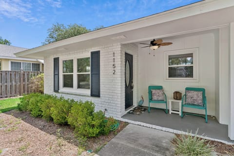 Charming white brick exterior with covered front porch featuring turquoise seating and a welcoming entrance in a peaceful residential setting.
