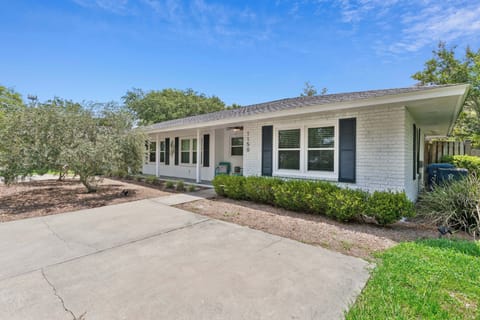 Mid-century ranch-style vacation home with white brick exterior, covered porch, and landscaped front yard, located in a quiet residential neighborhood.